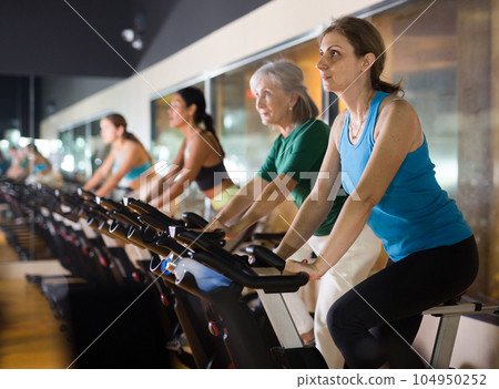 Woman riding stationary bike at fitness center 104950252