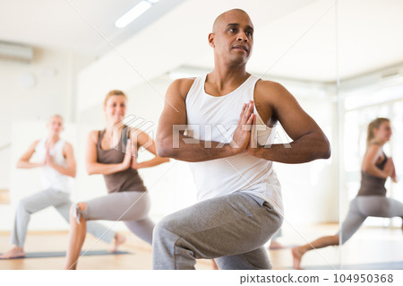 Hispanic man practicing Parvritta Parsvakonasana during group yoga training Hispanic man practicing Parvritta Parsvakonasana during group yoga training 104950368