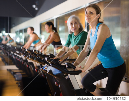 Woman riding stationary bike at fitness center 104950382