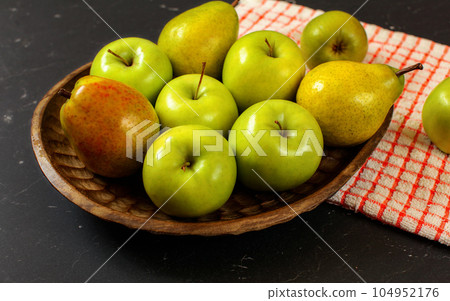 Wooden carved bowl with apples and pears with red chequered tablecloth on black board 104952176