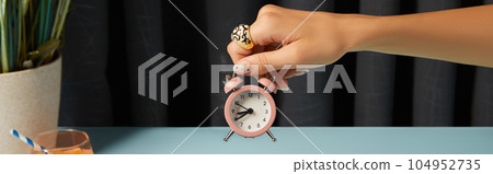 Beautiful groomed womans hand holding alarm clock over blue table. 104952735