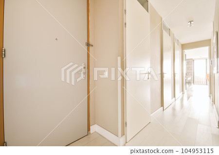 a long hallway with white walls and wood trim on the doors, which are closed to let light into the room 104953115