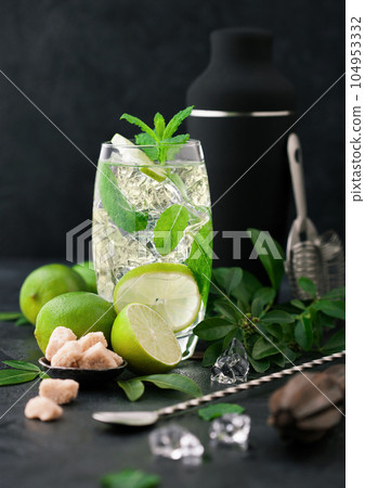Glass of Mojito cocktail with ice cubes mint and lime on black board with spoon 104953332