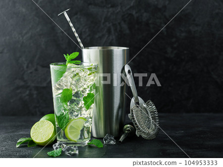 Glass of Mojito cocktail with ice cubes mint and lime on black board with fresh limes  104953333