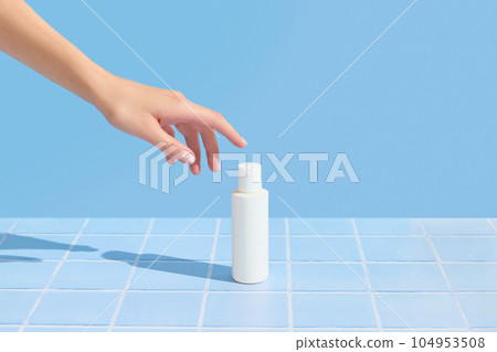 Womans hand holding white tube on blue tile background. Beauty treatment. Skin care routine 104953508