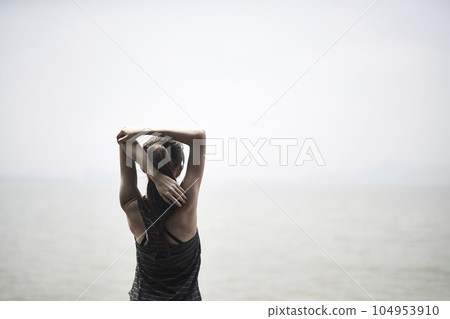 young asian adult woman stretching arms outdoors by the sea, rear view 104953910