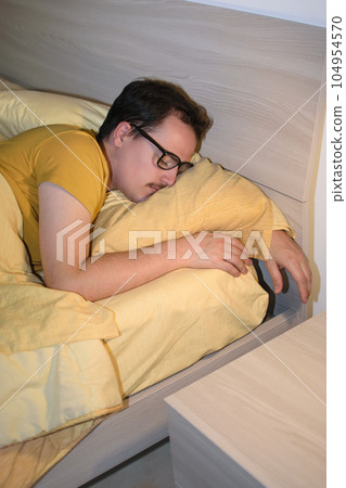 Young man with black eyeglasses sleeping turned in bed. 104954570