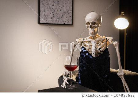 Skeleton in dress with wine sitting at table indoors 104955652