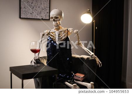 Skeleton in dress with wine sitting at table indoors Skeleton in dress with wine sitting at table indoors 104955653