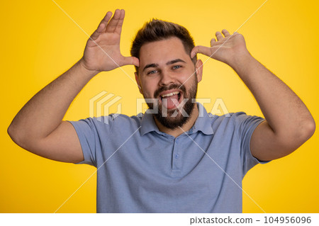 Comical funny caucasian man making playful silly facial expressions, fooling around, showing tongue 104956096