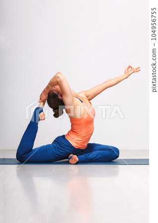 Woman doing Hatha yoga asana Eka pada rajakapotasana - one-legged king pigeon pose on yoga mat on yoga mat in studio on grey bagckground 104956755
