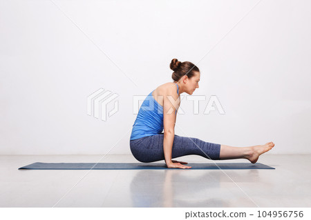 Woman doing Hatha asana Utpluti dandasana - lifted stuff pose on yoga mat on yoga mat in studio on grey bagckground Woman doing Hatha asana Utpluti dandasana - lifted stuff pose on yoga mat on yoga mat in studio on grey bagckground 104956756
