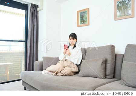 A young woman in plain clothes using a smartphone in the living room 104958409