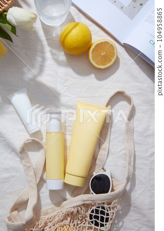 Cosmetic tube and pump bottle without label displayed with a mesh bag, sunglasses and fresh lemon. The vitamin C in Lemon (Citrus limon) is essential for the production of collagen Cosmetic tube and pump bottle without label displayed with a mesh bag, sunglasses and fresh lemon. The vitamin C in Lemon (Citrus limon) is essential for the production of collagen 104958865