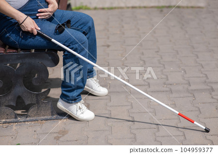 A blind pregnant woman sits on a bench and holds a folding tactile cane in her hands. A blind pregnant woman sits on a bench and holds a folding tactile cane in her hands. 104959377
