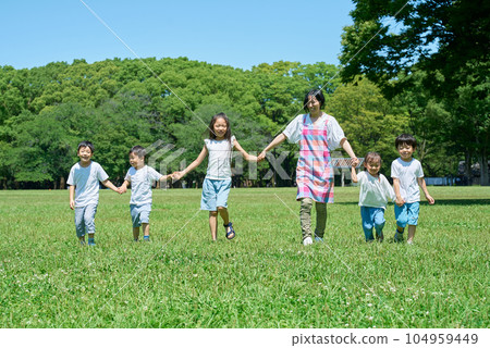 Children and women lined up holding hands in a green space Children and women lined up holding hands in a green space 104959449