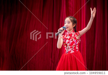 The Asian kid girl sing a song on stage at her school activity day, dress in Qipao style, red curtain background 104959811