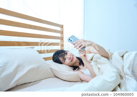 A woman using a smartphone in bed 104960005