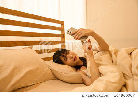 A woman using a smartphone in bed 104960007