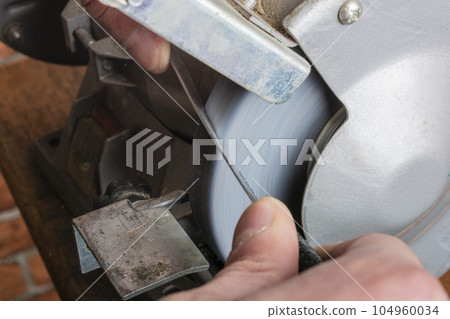 Knife sharpener and hand with blade on wooden table, closeup 104960034