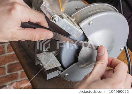 Knife sharpener and hand with blade on wooden table, closeup Knife sharpener and hand with blade on wooden table, closeup 104960035