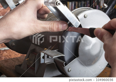Knife sharpener and hand with blade on wooden table, closeup Knife sharpener and hand with blade on wooden table, closeup 104960036