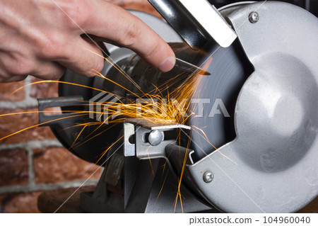 Knife sharpener and hand with blade on wooden table, closeup Knife sharpener and hand with blade on wooden table, closeup 104960040