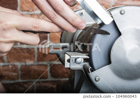 Knife sharpener and hand with blade on wooden table, closeup Knife sharpener and hand with blade on wooden table, closeup 104960043