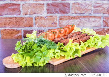 Lulya-kebab. Shish kebab on a stick, minced meat. Traditional Caucasian dish. On a cutting board, with green salad, ketchup, spices. 104960109