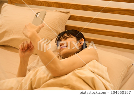 A woman using a smartphone in bed 104960197