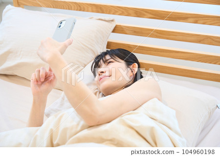 A woman using a smartphone in bed A woman using a smartphone in bed 104960198