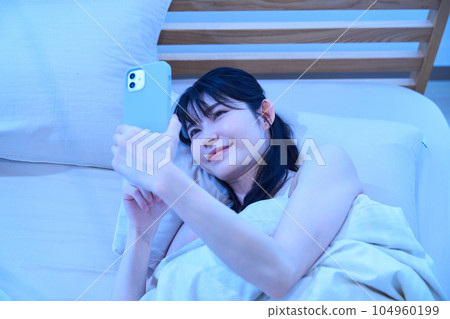 A woman using a smartphone in bed A woman using a smartphone in bed 104960199
