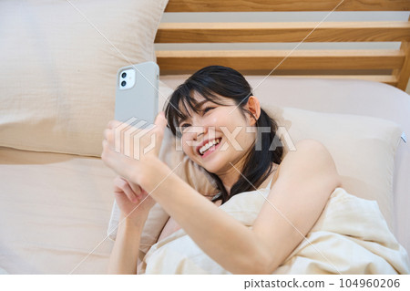A woman using a smartphone in bed 104960206