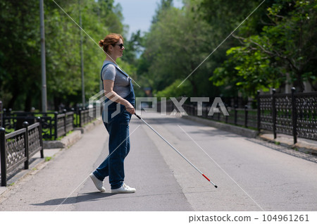 Blind pregnant woman crosses the street with the help of a tactile cane. Blind pregnant woman crosses the street with the help of a tactile cane. 104961261