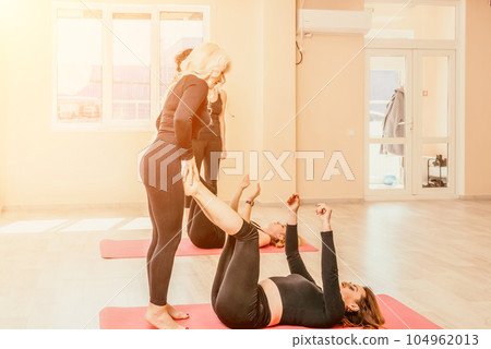 Well looking middle aged woman with black hair, fitness instructor in leggings and tops doing stretching and pilates on yoga mat near the mirror. Female fitness yoga routine concept. Healthy lifestyle Well looking middle aged woman with black hair, fitness instructor in leggings and tops doing stretching and pilates on yoga mat near the mirror. Female fitness yoga routine concept. Healthy lifestyle 104962013