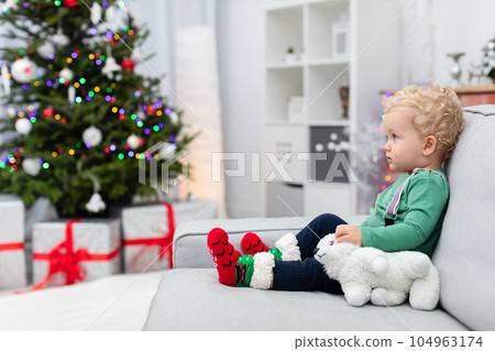 A young child sitting on a couch seen in profile against the backdrop of a Christmas tree A young child sitting on a couch seen in profile against the backdrop of a Christmas tree 104963174