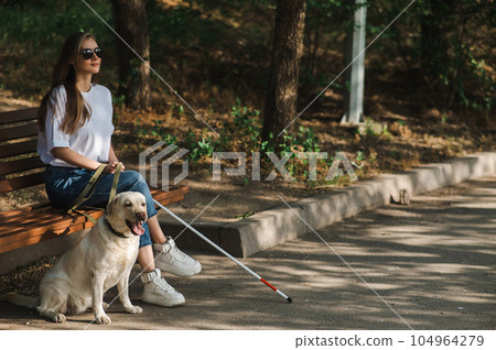 Blind caucasian woman sitting on bench with guide dog. Blind caucasian woman sitting on bench with guide dog. 104964279