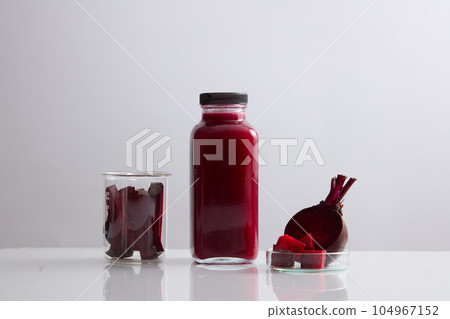 A glass bottle without label filled with beetroot juice. Beaker and petri dish of beetroot slices displayed. Beetroot (Beta vulgaris) may improve muscle power in people with heart failure 104967152