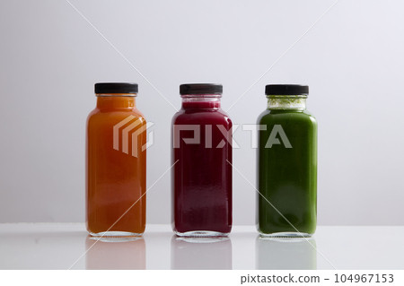 Front view of three blank label glass bottle filled with juice in orange, red and green color. Mockup design of healthy beverage brands. Organic juice concept 104967153