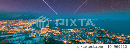 Naples, Italy. Skyline Cityscape In Evening Lighting. Tyrrhenian Sea And Landscape With Volcano Mount Vesuvius. Bold Bright Blue Azure Night Starry Sky With Glowing Stars. City In Night Illuminations 104969310