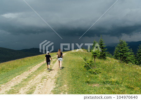 Mom with children walks in the mountains on the eve of a thunderstorm. People go down from the mountain to a safe place 104970640