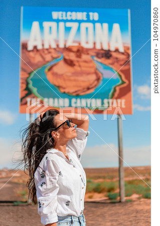 Beautiful woman on her trip to the USA on the background of Welcome to Arizona State border sign right in the Paje Canyon, USA Beautiful woman on her trip to the USA on the background of Welcome to Arizona State border sign right in the Paje Canyon, USA 104970860