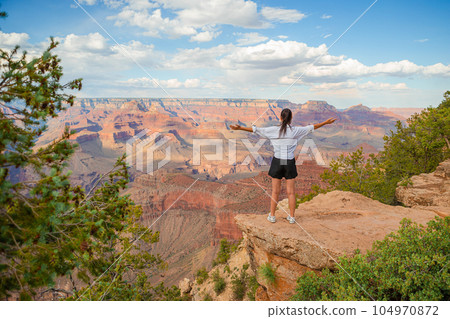 Happy young woman on a steep cliff taking in the amazing view over famous Grand Canyon on a beautiful sunny day, Grand Canyon National Park, Arizona, USA 104970872