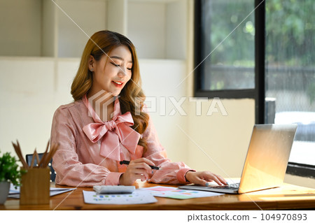 Beautiful asian economist woman typing business email, analyzing financial market on laptop Beautiful asian economist woman typing business email, analyzing financial market on laptop 104970893