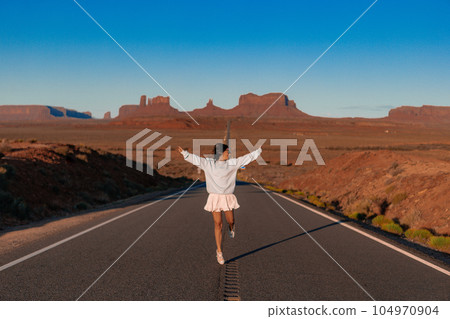 Happy young woman in white dress on the famous road to Monument Valley in Utah. Amazing view of the Monument valley. 104970904