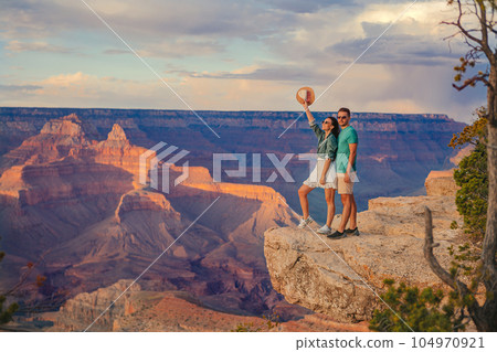 Happy young couple on a steep cliff taking in the amazing view over famous Grand Canyon on a beautiful sunny day, Grand Canyon National Park, Arizona, USA 104970921