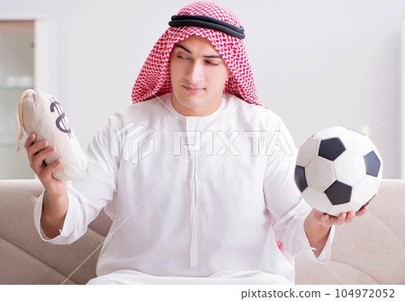 Young arab man watching football sitting on sofa 104972052
