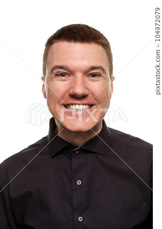 Handsome young man in a black shirt is making faces, while standing isolated on a white background Handsome young man in a black shirt is making faces, while standing isolated on a white background 104972079