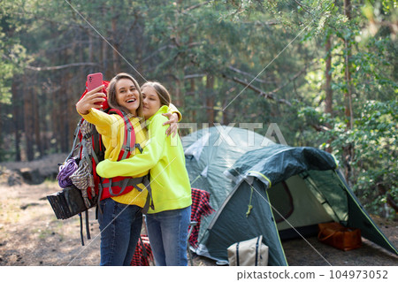 Mom with daughter taking a selfie in a forest camp. 104973052