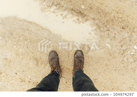 View from above on pair of trekking shoes in a mud, Hiking boots stuck in mud View from above on pair of trekking shoes in a mud, Hiking boots stuck in mud 104974297
